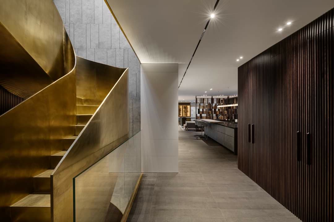 Brass spiral staircase with dark wood wall paneling by iKitchen Cabinetry