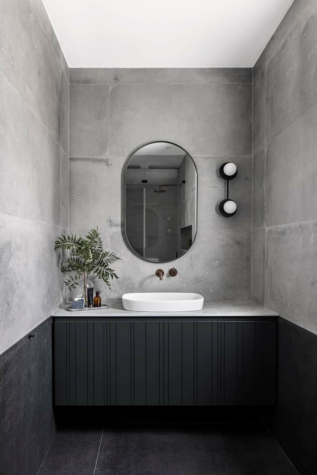 Concrete-finish bathroom with white vessel sink and oval mirror above a custom vanity by iKitchen Cabinetry