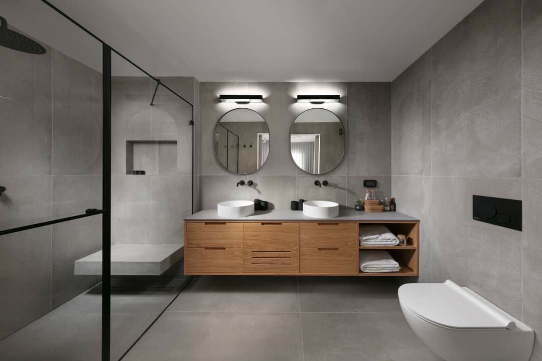 Walnut double vanity with round mirrors and stone counters by iKitchen Cabinetry